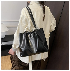 Close-up of a large black glossy tote bag with a small silver bow detail and dual straps