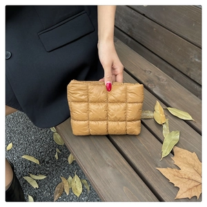 Close-up of khaki quilted puffer clutch bag on a wooden bench with autumn leaves detail