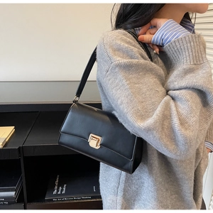 Detail of a black leather shoulder bag with a gold square clasp on a commuter model