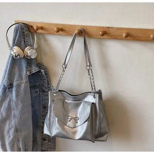 Close-up of a silver tote bag with metallic luster, metal bow detail, and chain strap