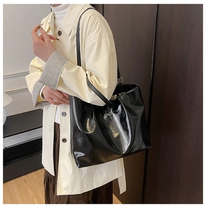 Detail of black glossy leather tote bag with metal bow pendant and shoulder strap detail