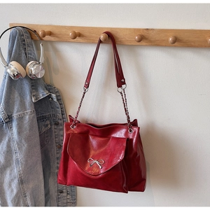 Detail of red faux leather tote bag with silver bow buckle hanging on a wooden rack