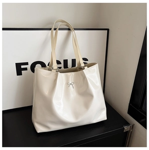 Close-up of cream white tote bag with silver metal bow detail and glossy leather texture