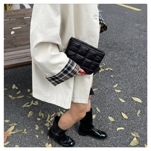 Street style shot of black quilted clutch bag paired with beige trench coat and boots