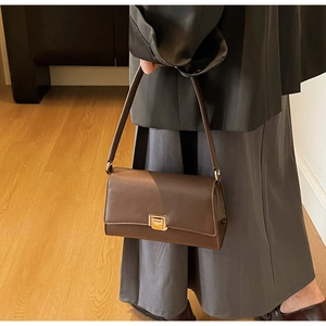 Brown leather baguette bag with gold buckle shown on shoulder of person in grey suit