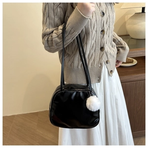 Detail of a shiny black faux leather shoulder bag with a white fluffy pompom keychain