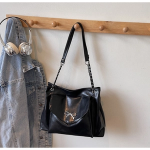 Close-up of black tote bag with silver bow detail and metal chain strap on wooden hook