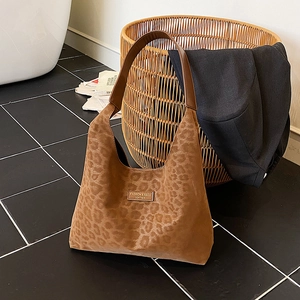 Classic leopard print tote bag with brown leather straps leaning against a woven basket