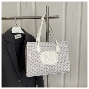 Close-up of white tote bag with embossed M letter pattern and metal display rack