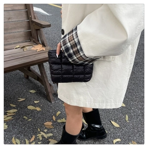 Street style shot of a black quilted clutch bag with grid stitching and metallic finish