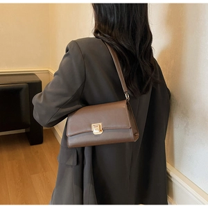 Detailed shoulder view of a brown matte leather bag with a gold metal lock and long strap