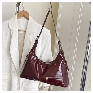 Detail of burgundy patent leather hobo bag with gold hardware and front zipper pocket