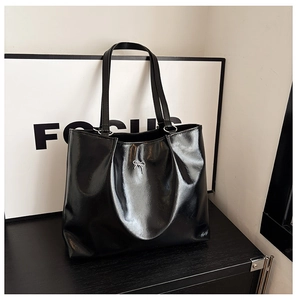 Detail shot of black glossy leather tote bag featuring a silver metal bow accent