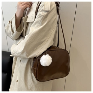 Detail of a brown leather toiletry bag with white plush ball charm worn with a beige coat