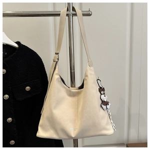 Detail of cream hobo bag featuring adjustable strap and a cute tricolor dog charm