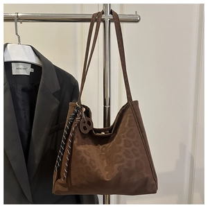 Détail du sac cabas en daim léopard avec nœud tissé et breloque ronde sur le côté