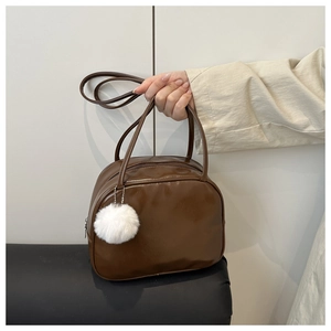 Detail of vintage brown leather wash bag with a white fluffy ball charm and handle