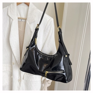Detail of black patent leather crescent bag with gold zippers and adjustable strap