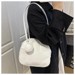 Detail of white PU leather travel bag with plush ball charm on black coat