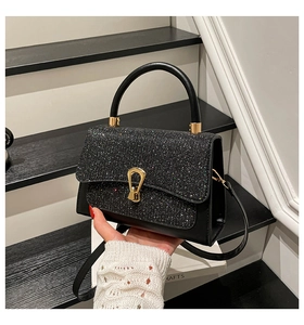 Detail einer schicken schwarzen Ledertasche mit glitzernder Klappe und goldenem U-Drehverschluss