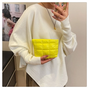 Close-up of bright yellow quilted checkered clutch bag held by a model in casual style