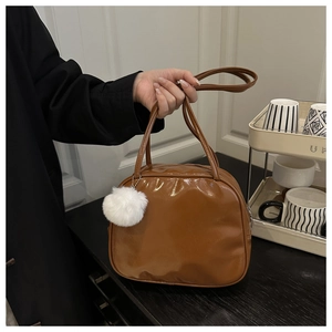 Close-up of brown glossy PU leather travel wash bag with double handles and white pom-pom