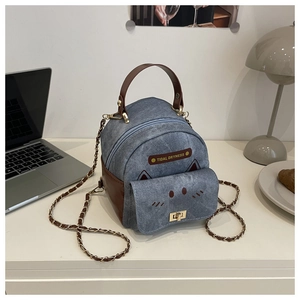 Detail of denim mini backpack with cat pocket and leather trim on a desk