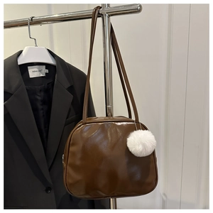 Close-up of brown glossy PU leather tote bag with a white faux fur pompom charm