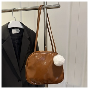 Detail of glossy brown faux leather shoulder bag with white fluffy charm on a hanger