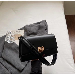 Detail of minimalist black baguette bag with gold square clasp on grey blazer background