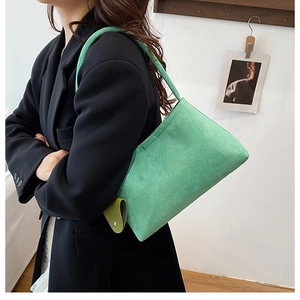 Detail of mint green suede shoulder bag texture worn with a black suit jacket