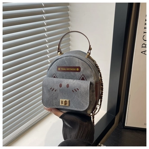 Detail of grey denim cat-themed mini backpack with gold metal lock and leather label