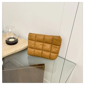 Detail of quilted mustard yellow nylon handbag displayed on a glass tabletop with marble tray