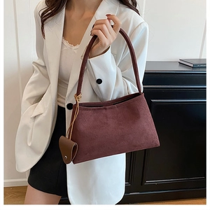 Detail view of burgundy suede shoulder bag featuring a brown heart-shaped charm accessory