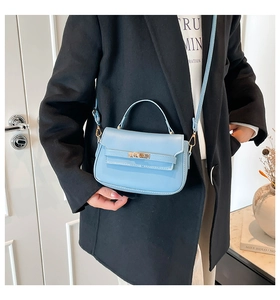 Detail view of light blue leather saddle bag with golden metal buckle and top handle