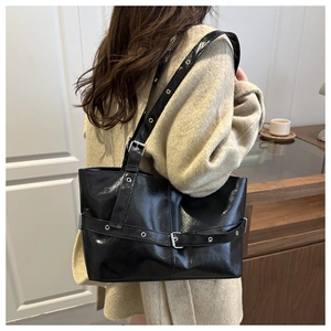 Chic black glossy tote bag with metal eyelets worn by a model in a cozy indoor setting