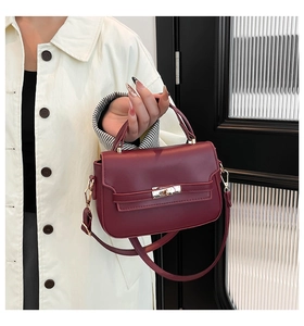 Close-up of wine red saddle bag with gold metal lock worn by model in beige coat