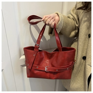 Detail of dark red tote bag with silver buckle strap and metal eyelets on soft PU leather