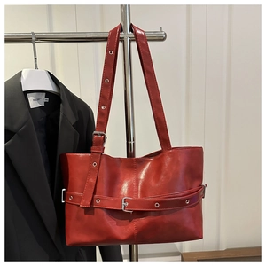 Detail of red faux leather tote bag showing glossy finish and decorative belt buckle