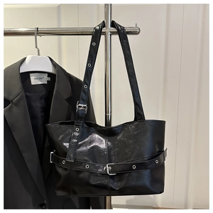 Close-up of black high-gloss tote bag with silver eyelets and moto-style buckle details