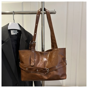 Detail of dark brown tote bag with decorative belt and metallic eyelets on polished leather