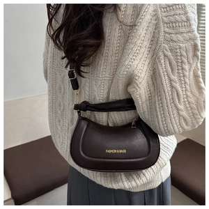 Detail of dark brown leather crescent bag with gold lettering on a white knit sweater