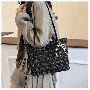 Detail einer Tweed-Schultertasche mit Perlen-Schleifen-Anhänger und Lederriemen