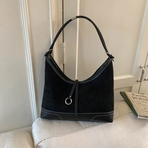 Sac hobo rétro en daim noir avec surpiqûres blanches sur un canapé minimaliste