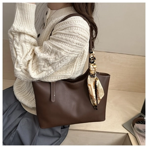 Detail of a large brown tote bag with contrast stitching and a decorative silk scarf accessory