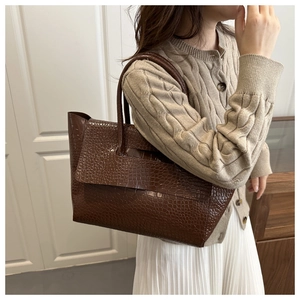 Detail of dark brown tote bag featuring glossy crocodile texture and sturdy handles