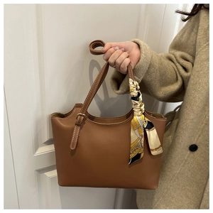 Brown leather tote bag with silk scarf detail held by model in beige coat