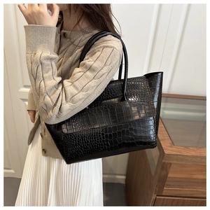 Close-up of black crocodile pattern leather tote bag worn by a model in interior setting