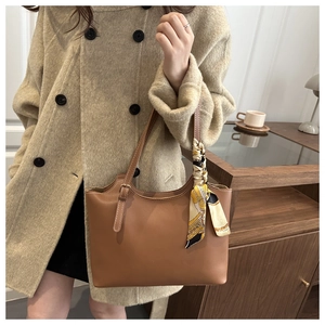 Close-up of brown leather tote bag featuring contrast stitching and yellow patterned scarf