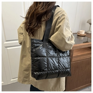 Detail of large black quilted tote bag with shiny finish and wide nylon shoulder strap